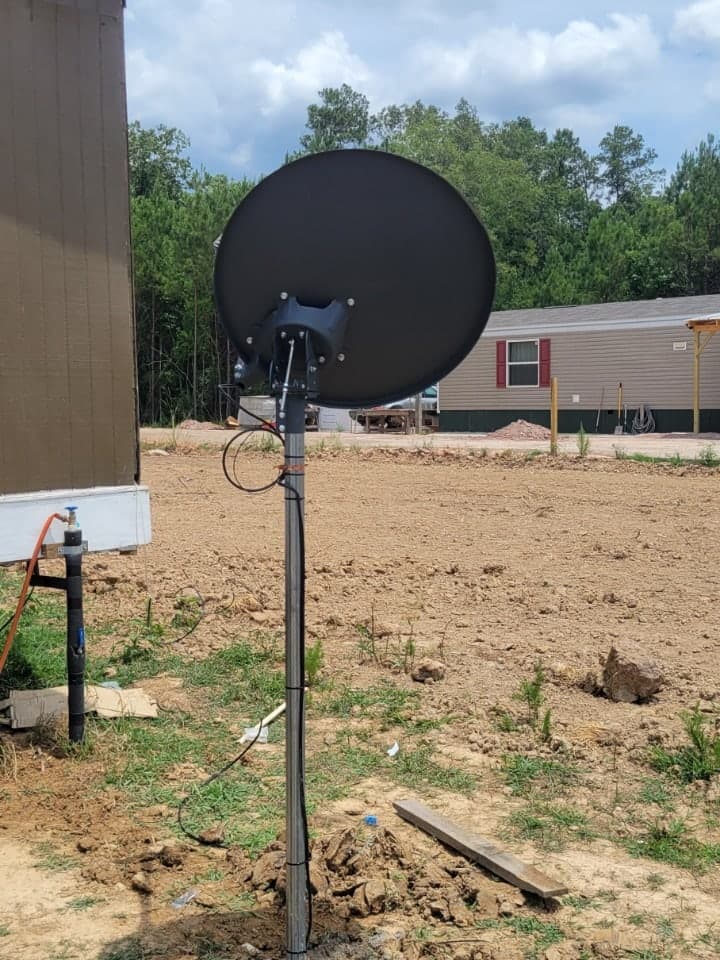 Antena de plato montada en un poste de acero junto a una casa en una propiedad rural